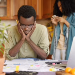 stressed-young-african-male-doing-paperwork-home-holding-hands-head_273609-9219